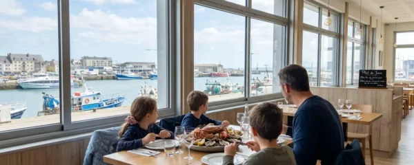 Une famille vue de dos attablée près d'une grande baie vitrée donnant sur le port de Cherbourg, plateau de fruits de mer au centre de la table