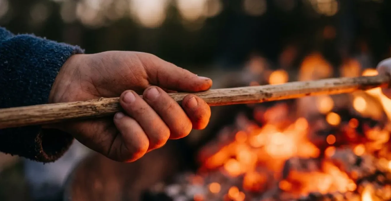 Main d'enfant tenant une brochette devant des braises rougeoyantes au crépuscule