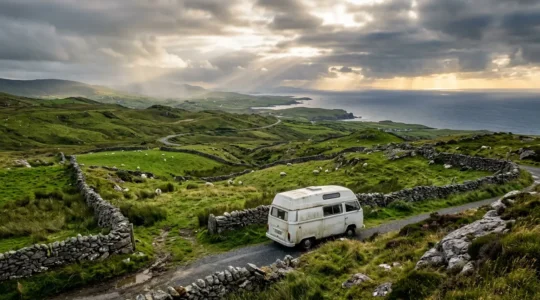 Campeur devant un van aménagé contemplant un paysage verdoyant irlandais typique avec des murets de pierre et des moutons, ambiance de voyage authentique