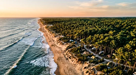 Vue aerienne combinant ocean Atlantique avec surfeurs, foret de pins des Landes et emplacement de camping nature au coucher du soleil